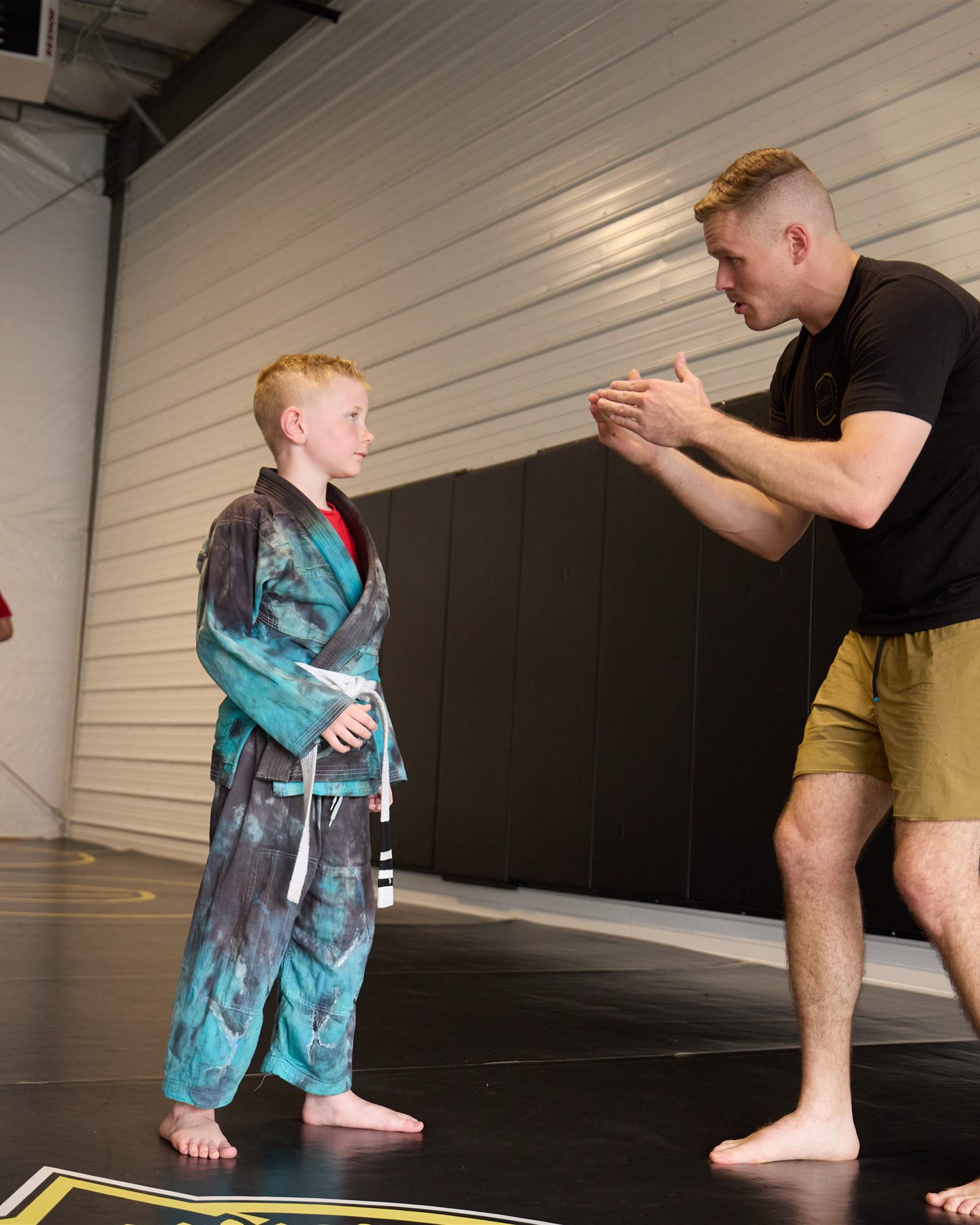 A coach kneeling at eye level to walk a young wrestler through a technique